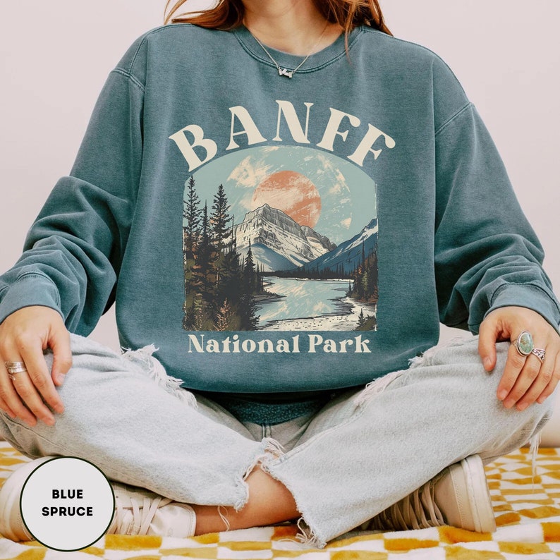 May include: A blue sweatshirt with a vintage-style graphic of a mountain landscape and the text "Banff National Park".
