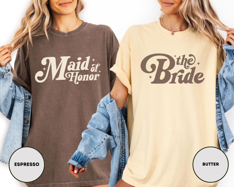 May include: Two oversized t-shirts are shown, one in espresso and the other in butter. The espresso shirt features the text "Maid of Honor" in a retro font. The butter shirt says "the Bride". Both are casual and suitable for a bridal party.