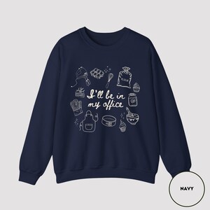 May include: Navy blue sweatshirt with white line art of baking tools and the text "I'll be in my office." The design includes a mixer, whisk, flour sack, and other kitchen items. The sweatshirt is a comfortable, casual style.