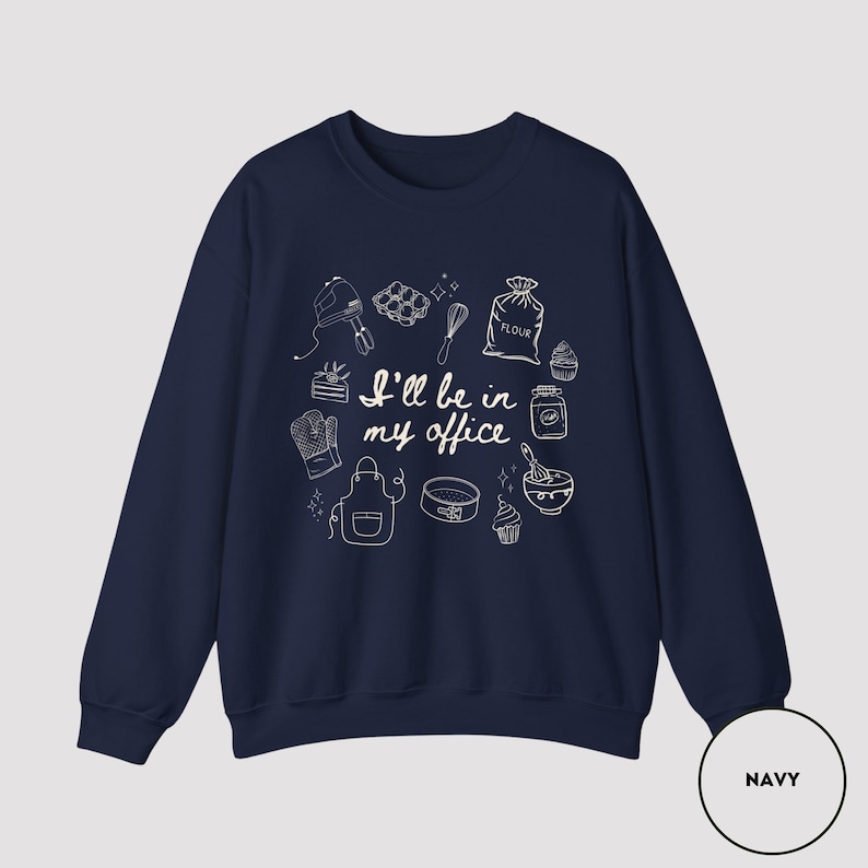 May include: Navy blue sweatshirt with white line art of baking tools and the text "I'll be in my office." The design includes a mixer, whisk, flour sack, and other kitchen items. The sweatshirt is a comfortable, casual style.