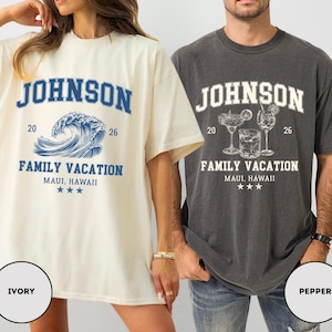 K&ouml;nnte beinhalten: Zwei kurz&auml;rmelige T-Shirts, eines in Elfenbein und eines in Pfeffer, mit dem Namen "JOHNSON" &uuml;ber "FAMILY VACATION, MAUI, HAWAII." Das elfenbeinfarbene Shirt hat eine blaue Wellengrafik, w&auml;hrend das pfefferfarbene Shirt Cocktail-Illustrationen hat. Beide Shirts enthalten die Jahre "20" und "26".