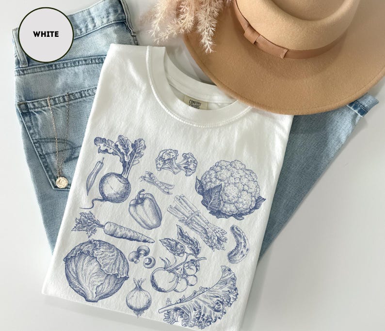 May include: White t-shirt with a blue ink illustration of various vegetables, including a beet, carrot, and cauliflower. The shirt is paired with light blue jeans and a tan hat. The word "WHITE" is in a white circle.