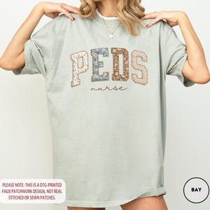 May include: A light green t-shirt with the word "PEDS" in a patchwork design, with the word "nurse" below it. The shirt has short sleeves and a relaxed fit. The text "PLEASE NOTE: THIS IS A DTG-PRINTED FAUX PATCHWORK DESIGN, NOT REAL STITCHED OR SEWN PATCHES." is at the bottom.