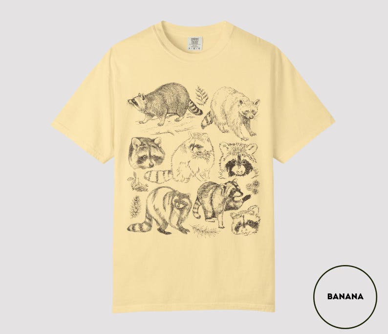 Op de afbeelding: Bananegele t-shirt met een reeks gedetailleerde wasbeer illustraties in zwarte inkt. Het ontwerp bevat verschillende poses en close-ups van de dieren. Het shirt heeft een klassieke ronde hals en korte mouwen.