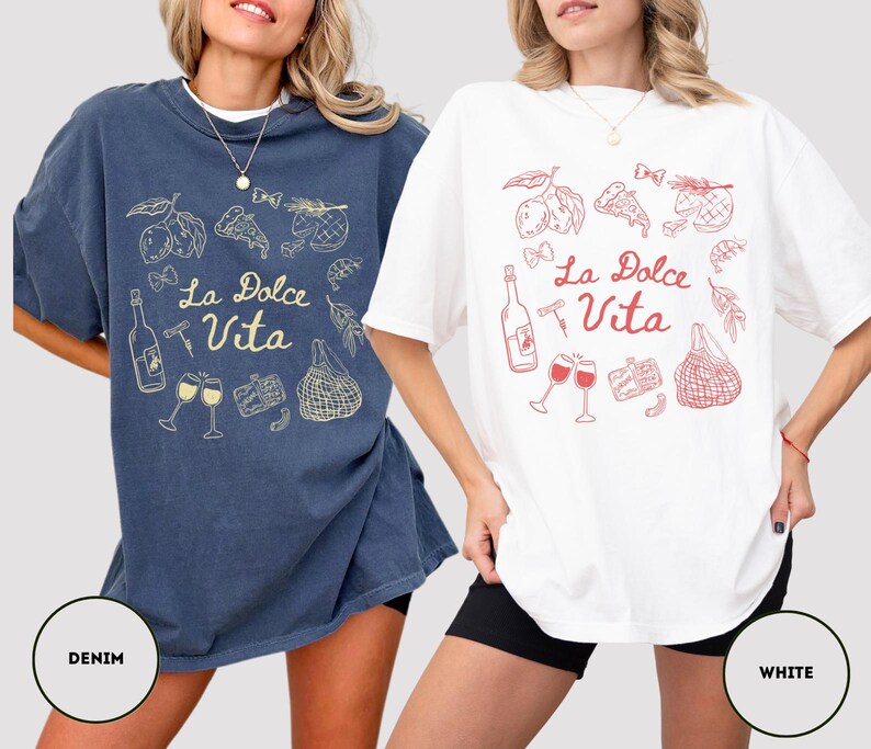 May include: Two oversized t-shirts, one denim blue and one white, each featuring a "La Dolce Vita" design. The design includes illustrations of lemons, pizza, wine bottles, glasses, and a shopping bag. The white shirt has a red design, while the denim shirt has a gold design.