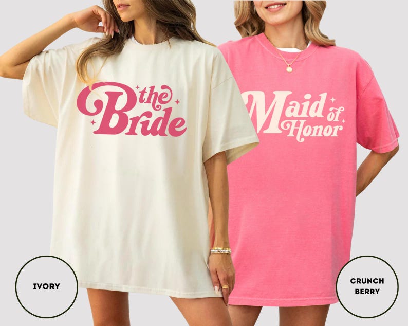 May include: Two oversized t-shirts. One is ivory with the text "the Bride" in pink script. The other is pink with the text "Maid of Honor" in white script. Both shirts have short sleeves and a crew neck.