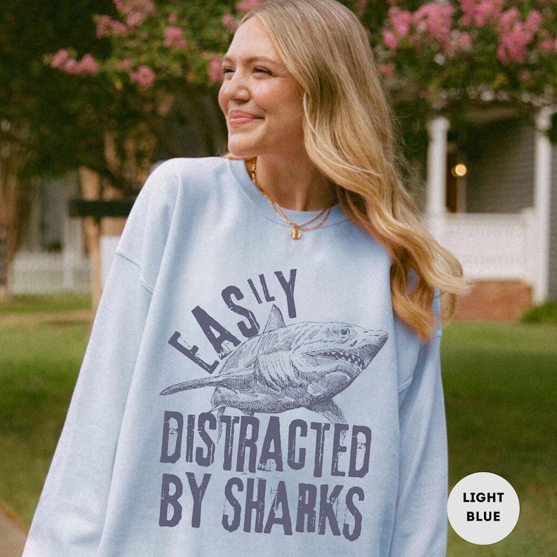 May include: Light blue sweatshirt with a graphic of a shark and the text "Easily Distracted By Sharks".