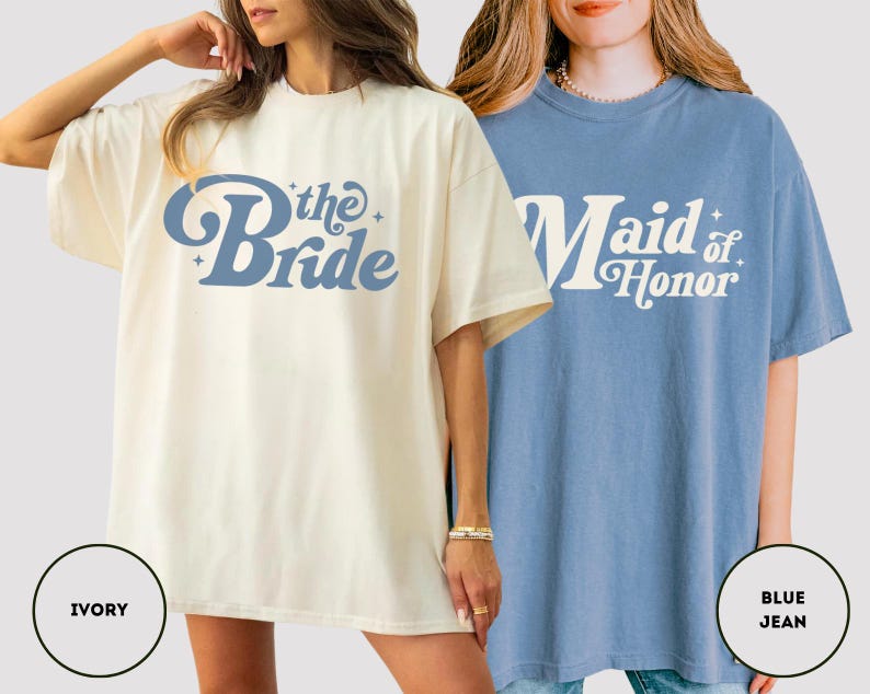 May include: Two oversized t-shirts are shown, one ivory and one blue. The ivory shirt features "the Bride" in blue script, while the blue shirt says "Maid of Honor" in white. Both are short-sleeved and have a retro design, ideal for a bridal party.