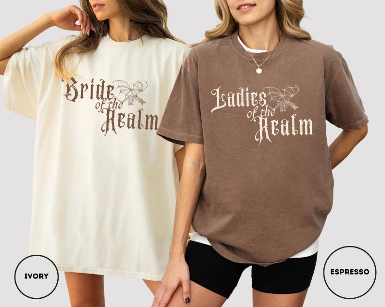 May include: Two oversized t-shirts, one ivory and one espresso, featuring the text "Bride of the Realm" and "Ladies of the Realm" in a decorative font. The shirts have a relaxed fit and short sleeves.