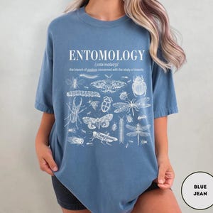 May include: A blue t-shirt with a white print of the word "ENTOMOLOGY" and a definition of the word. The print also includes a variety of insects, including butterflies, beetles, and dragonflies.