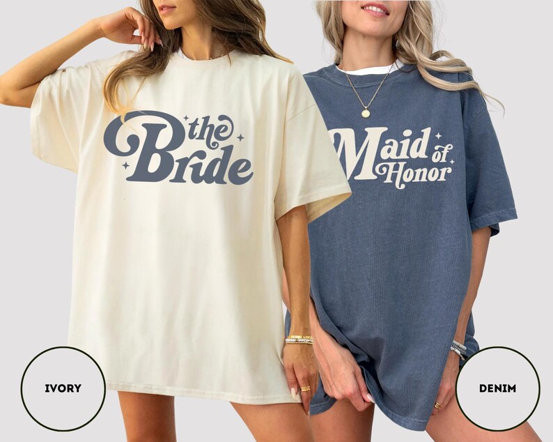 May include: Two oversized t-shirts, one ivory and one denim blue. The ivory shirt has "the Bride" in a retro font. The denim shirt says "Maid of Honor" in a similar style. Both are short-sleeved and suitable for a bridal party.