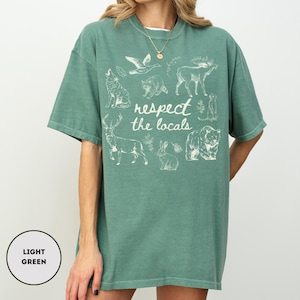May include: Light green t-shirt with a crew neck and short sleeves. The shirt features a white graphic of various animals and the text "respect the locals". The shirt is made of a soft, comfortable material.