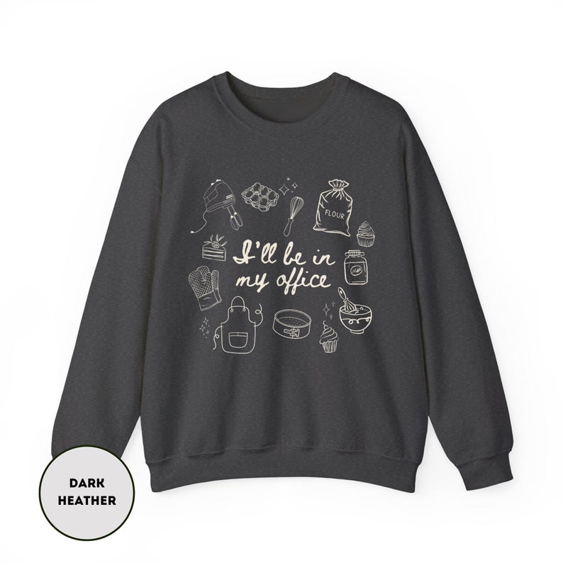 May include: Dark heather gray sweatshirt with a white graphic of baking tools and the text "I'll be in my office." The design includes a mixer, whisk, oven mitt, apron, and other kitchen items. A round label at the bottom left says "Dark Heather."