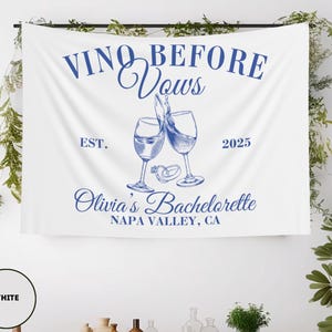 Peut inclure: Banni&egrave;re blanche avec du texte bleu qui dit "Vino Before Vows Est. 2025 Olivia's Bachelorette Napa Valley, CA". La banni&egrave;re repr&eacute;sente deux verres &agrave; vin avec une bague sur la tige de chaque verre.