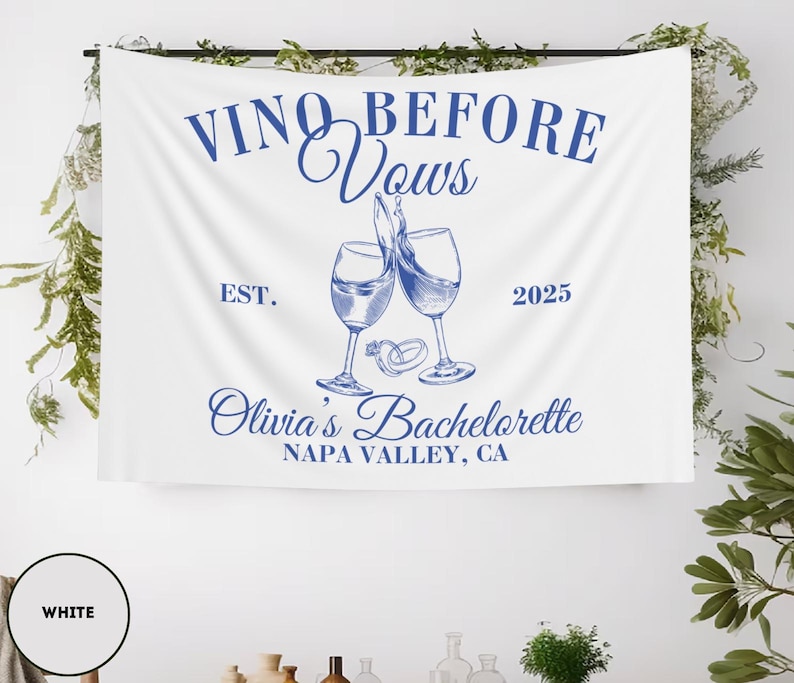 Peut inclure: Banni&egrave;re blanche avec du texte bleu qui dit "Vino Before Vows Est. 2025 Olivia's Bachelorette Napa Valley, CA". La banni&egrave;re repr&eacute;sente deux verres &agrave; vin avec une bague sur la tige de chaque verre.