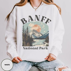 May include: White sweatshirt with a graphic design of a mountain landscape and the text "Banff National Park".