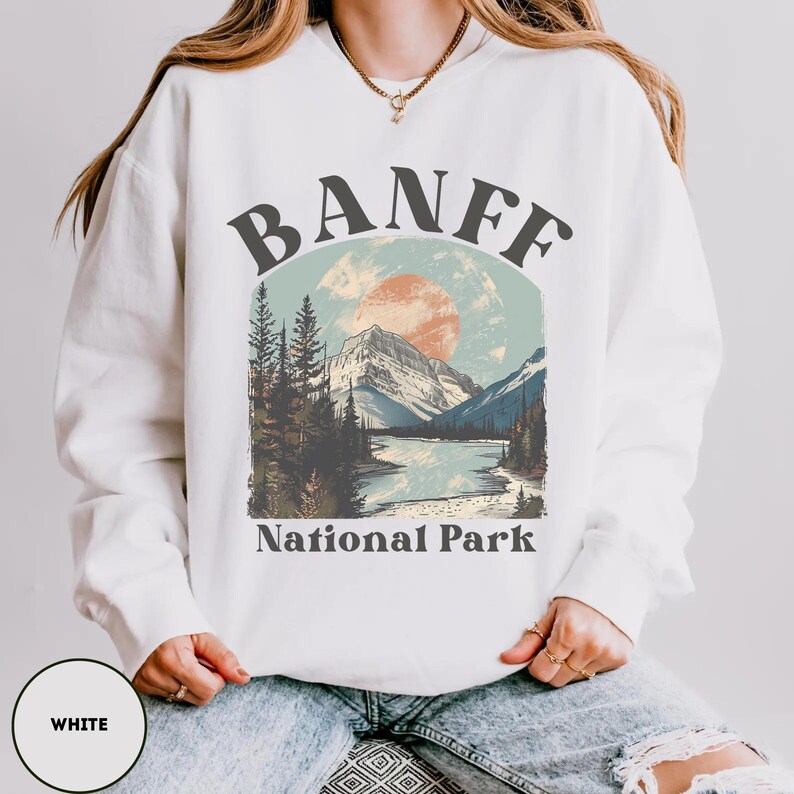 May include: White sweatshirt with a graphic design of a mountain landscape and the text "Banff National Park".