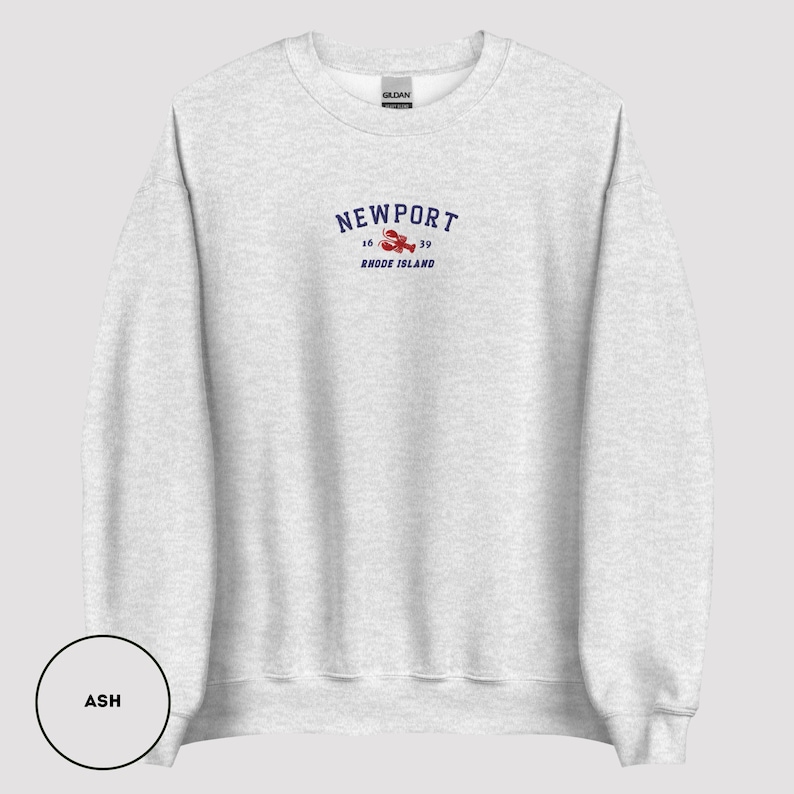 May include: Light grey sweatshirt featuring the word "NEWPORT" in navy blue arched text, a red lobster graphic, and the text "16 39 RHODE ISLAND". The sweatshirt is a Gildan brand.