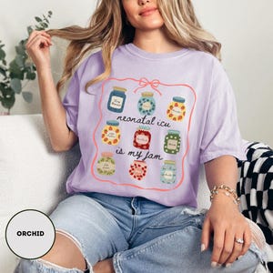 May include: A light purple t-shirt with a graphic of jam jars and the text "neonatal icu is my jam". The shirt is made of a soft material and is a comfortable fit.