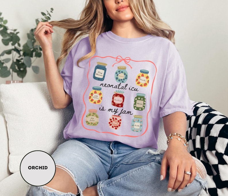 May include: A light purple t-shirt with a graphic of jam jars and the text "neonatal icu is my jam". The shirt is made of a soft material and is a comfortable fit.