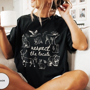 May include: Black t-shirt with a white graphic of various animals and the text "respect the locals." The design includes a wolf, raccoon, moose, deer, rabbit, and bear. The shirt is a relaxed fit.
