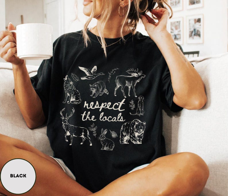 May include: Black t-shirt with a white graphic of various animals and the text "respect the locals." The design includes a wolf, raccoon, moose, deer, rabbit, and bear. The shirt is a relaxed fit.