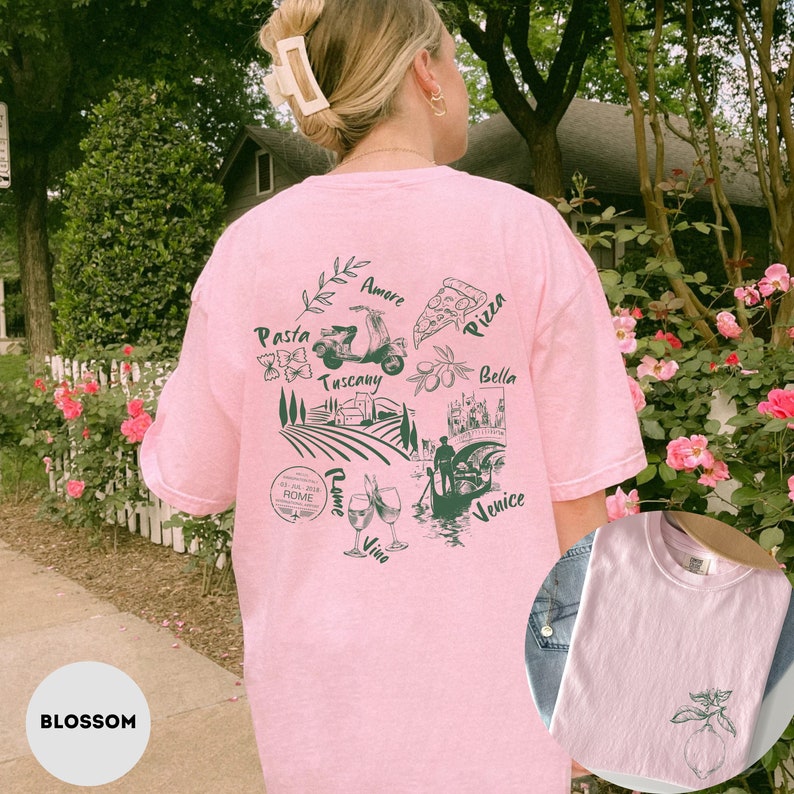 May include: Pink t-shirt with a green graphic of Italian imagery, including a scooter, pizza, and the words "Pasta," "Tuscany," "Rome," and "Venice." The shirt also features a small lemon graphic on the front. The word "Blossom" is at the bottom.