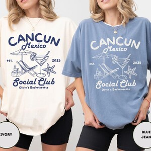 May include: Two oversized t-shirts with a blue graphic design that says "Cancun Mexico est. 2025 Social Club Olivia's Bachelorette". The graphic includes a beach umbrella, lounge chairs, and a cocktail glass. The t-shirts are shown in two colors: ivory and blue jean.