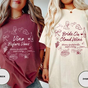 May include: Two t-shirts with a bachelorette party theme. The shirt on the left is brick red with white text that says "Vino Before Vows" and has a wine glass, bottle of wine, and other wine-related graphics. The shirt on the right is ivory with burgundy text that says "Bride On Cloud Wine" and has a wine glass, bottle of wine, and other wine-related graphics.