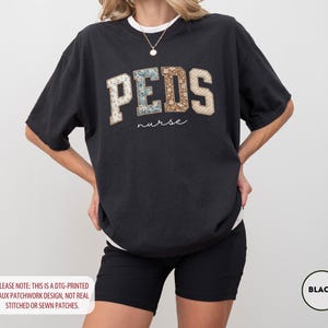 May include: Black t-shirt with the word "PEDS" in a faux patchwork design, with the word "nurse" underneath. The shirt is a relaxed fit and has a white crew neck collar. The text "PLEASE NOTE: THIS IS A DTG-PRINTED FAUX PATCHWORK DESIGN, NOT REAL STITCHED OR SEWN PATCHES." is at the bottom.