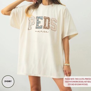 May include: Ivory-colored oversized t-shirt with the word "PEDS" in a patchwork design, and the word "nurse" in a script font. The shirt has short sleeves and a relaxed fit. The text "PLEASE NOTE: THIS IS A DTG-PRINTED FAUX PATCHWORK DESIGN, NOT REAL STITCHED OR SEWN PATCHES." is also visible.