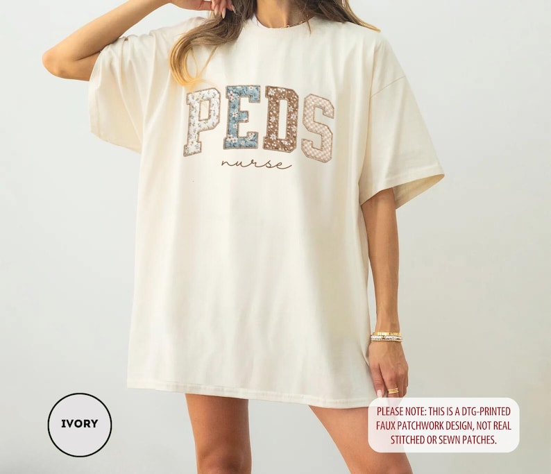 May include: Ivory-colored oversized t-shirt with the word "PEDS" in a patchwork design, and the word "nurse" in a script font. The shirt has short sleeves and a relaxed fit. The text "PLEASE NOTE: THIS IS A DTG-PRINTED FAUX PATCHWORK DESIGN, NOT REAL STITCHED OR SEWN PATCHES." is also visible.