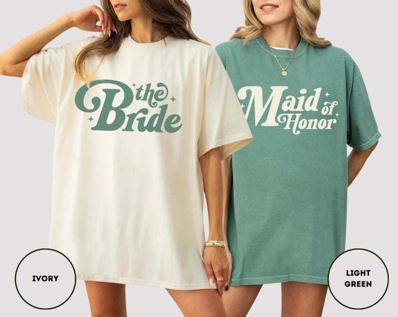 May include: Two oversized t-shirts, one ivory and one light green. The ivory shirt has the text "the Bride" in a retro font. The light green shirt says "Maid of Honor". Both shirts are short-sleeved.
