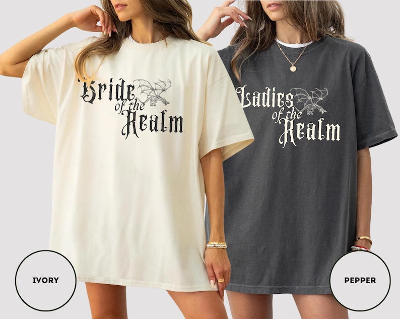 May include: Two oversized t-shirts, one ivory and one pepper, featuring the text "Bride of the Realm" and "Ladies of the Realm" in a gothic font with a dragon illustration. The shirts have short sleeves and a relaxed fit.
