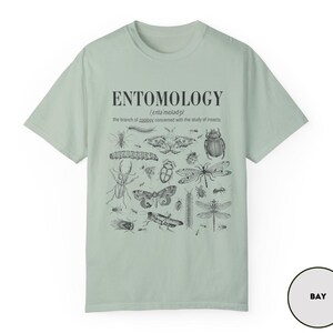 May include: A light green t-shirt with a black and white illustration of various insects. The text "ENTOMOLOGY" is printed in black at the top of the shirt, with the definition of the word below.