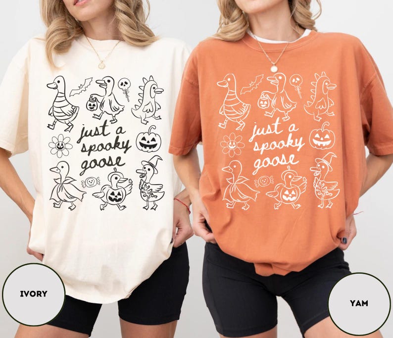 May include: Ivory and yam-colored t-shirts with a Halloween-themed graphic. The graphic features cartoon geese in costumes, a pumpkin, and the text "just a spooky goose". The shirts are oversized and casual.