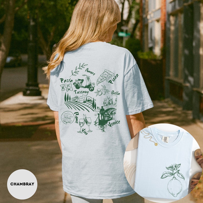 May include: Light blue t-shirt with a green illustration of Italian landmarks and food, including pasta, pizza, and a Vespa. The shirt also features the words "Pasta", "Pizza", "Tuscany", "Bella", "Venice", "Rome", "Amore", and "Vino". A smaller image of a lemon is on the front.