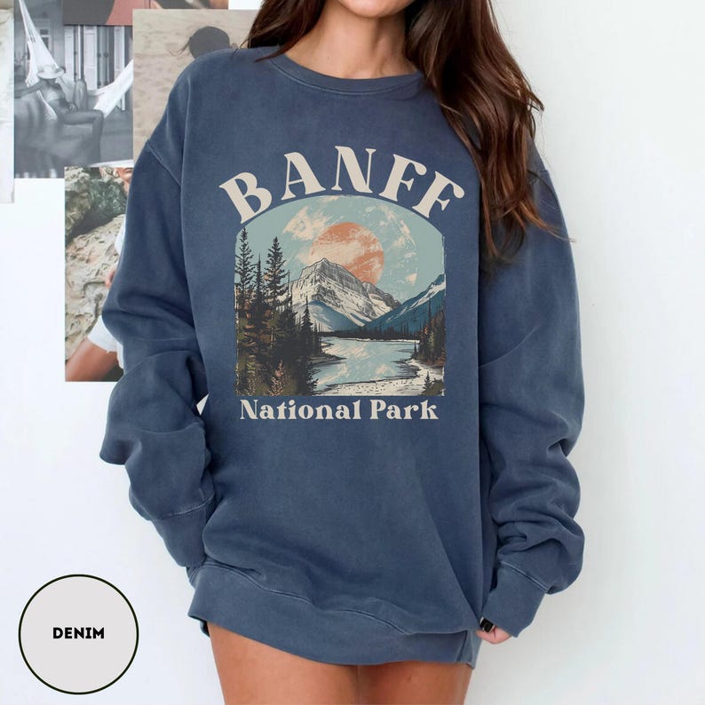 May include: A blue denim sweatshirt with a vintage-style graphic of a mountain landscape and the text "Banff National Park".