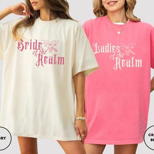 May include: Two oversized t-shirts, one ivory and one pink, with the text "Bride of the Realm" and "Ladies of the Realm" in a decorative font. The ivory shirt has a matching ivory circle with the word "IVORY". The pink shirt has a matching pink circle with the words "CRUNCH BERRY".