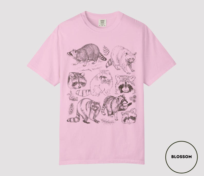 Op de afbeelding: Lichtroze T-shirt met een gedetailleerde illustratie van wasberen in verschillende poses en maten. De afbeelding is in grijstinten en zwart, wat een vintage esthetiek cre&euml;ert. Het shirt heeft een klassieke ronde hals en korte mouwen.