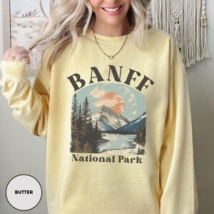 May include: A yellow sweatshirt with a vintage-style graphic of a mountain range and the text "BANFF National Park".