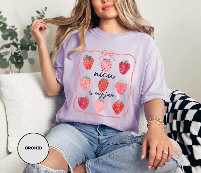 May include: A light purple t-shirt with a strawberry graphic and the text "nicu is my jam". The graphic features nine strawberries in various shades of red and pink, framed by a pink border.