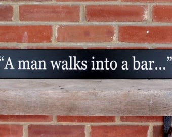 May include: A black wooden sign with white text that reads "A man walks into a bar..."