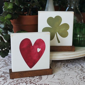 May include: Two wooden signs with a heart and a shamrock painted on them. The heart is red and the shamrock is green. The signs are on small wooden stands.
