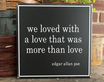 Puede incluir: Un letrero de madera negro con texto blanco que dice "we loved with a love that was more than love" y "edgar allan poe" en una fuente más pequeña.