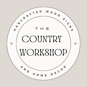 Puede incluir: Logotipo circular con el texto "THE COUNTRY WORKSHOP" en fuente serif, rodeado por las palabras "HANDCRAFTED WOOD SIGNS" y "AND HOME DECOR". El logotipo es blanco con contorno negro sobre un fondo beige claro.