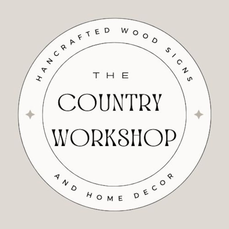 Puede incluir: Logotipo circular con el texto "THE COUNTRY WORKSHOP" en fuente serif, rodeado por las palabras "HANDCRAFTED WOOD SIGNS" y "AND HOME DECOR". El logotipo es blanco con contorno negro sobre un fondo beige claro.