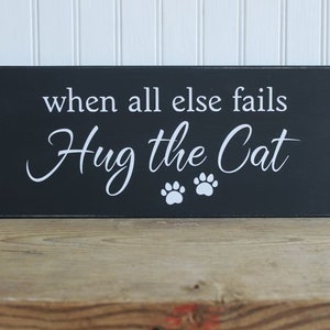 Black wood sign with white lettering saying When all else fails Hug the Cat.  Two white cat paw prints.  Sign measures 6x14 inches.