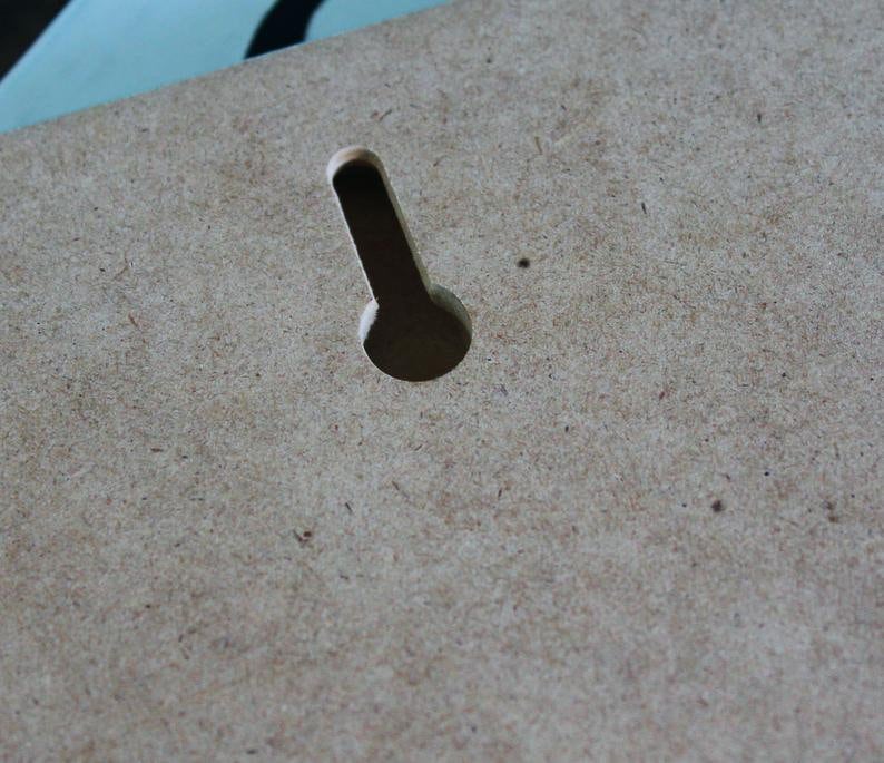 May include: A close-up of a light brown wooden surface with a small, rectangular hole cut out of it. The hole is centered in the image and is about 1 inch long and 1/2 inch wide.
