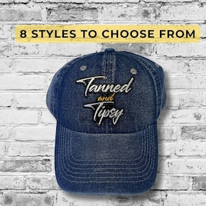 May include: A blue denim baseball cap with the embroidered text "Tanned and Tipsy" in white script. The cap has a curved brim and adjustable strap. The image also includes the text "8 Styles to Choose From" in a yellow box.